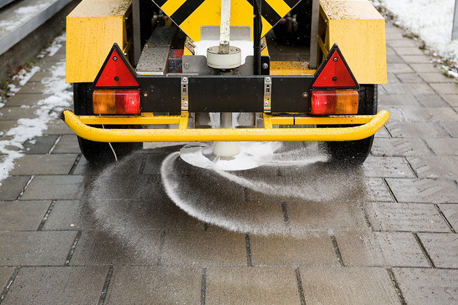 A yellow commercial salting vehicle laying salt on a residential or commercial walkway in Springfield, IL after snow removal service.