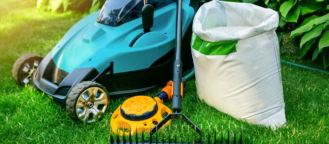 Blue commercial lawn mowing machine, a yellow irrigation system, rake, and white debris cleanup bag for spring yard cleaning in Springfield, IL.